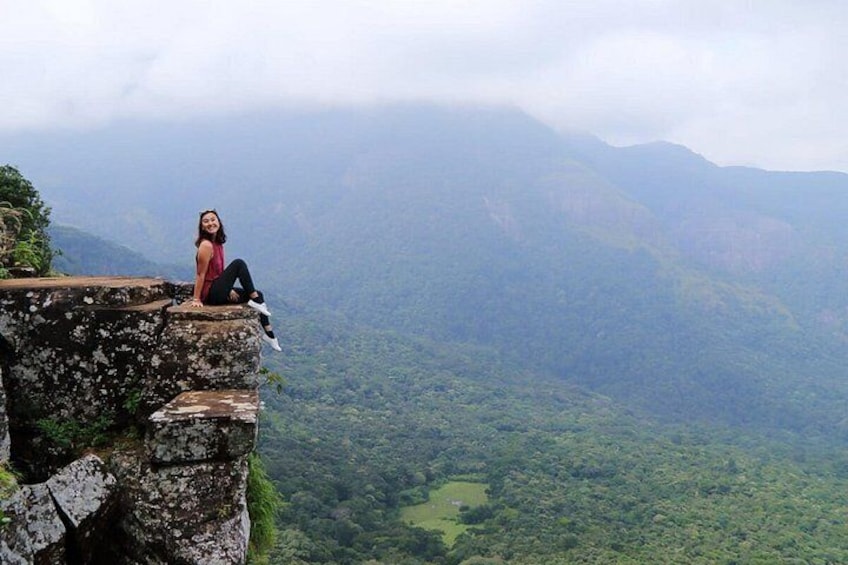 Una persona sentada al borde de un acantilado con vistas a un paisaje montañoso. 1