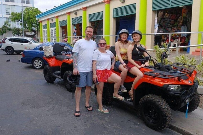 Een groep mensen op een quad, een gebouw met groene zuilen en een geparkeerde auto. 1
