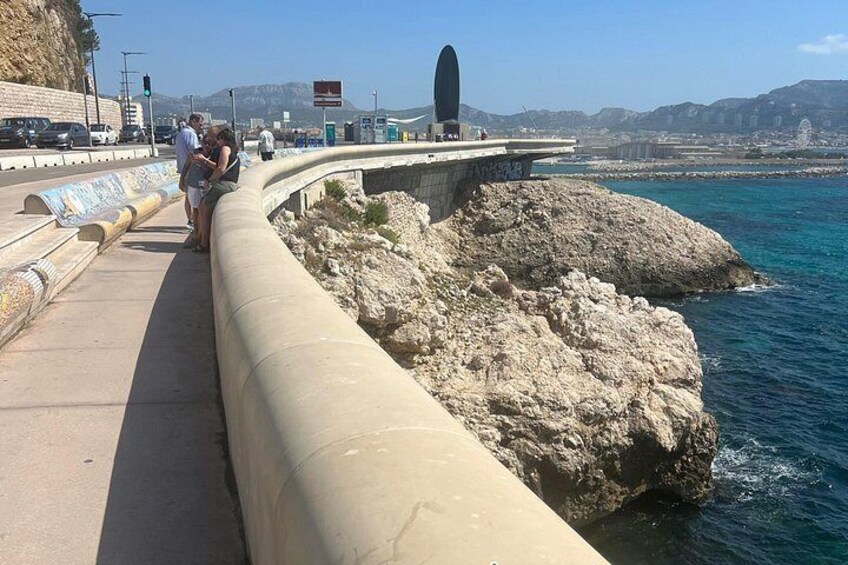 En strandpromenad längs kusten med folk som promenerar, en bro och en stenig strand. 1