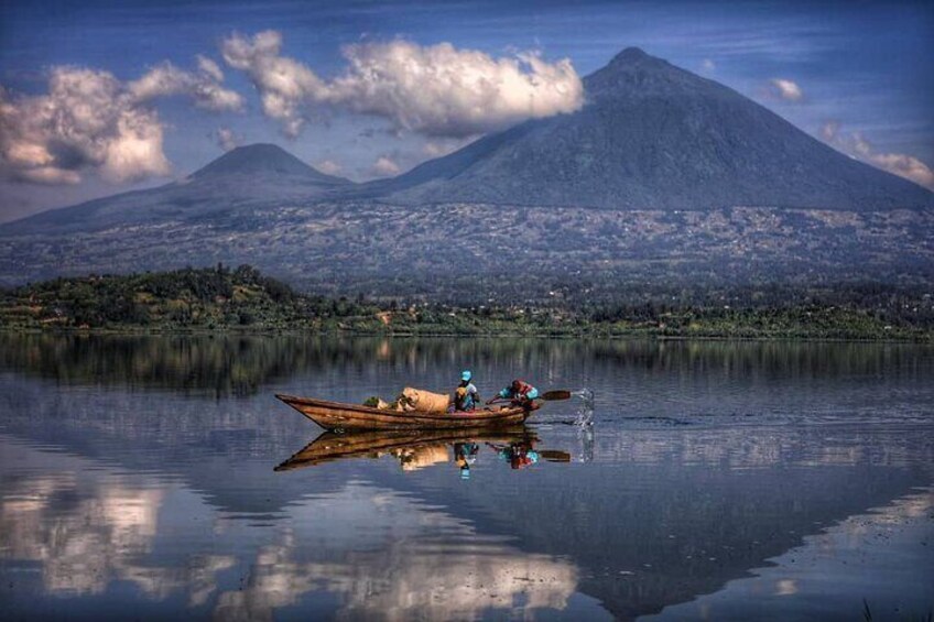 A calm lake with a wooden boat and two people rowing, a mountain in the background, and a clear reflection of the scene. 2