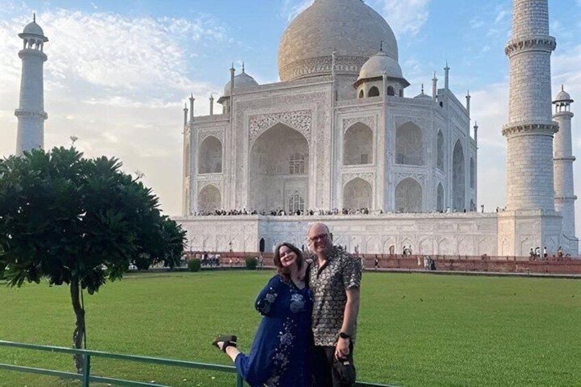 A couple posing in front of the Taj Mahal with a green lawn and a tree to the left. 5