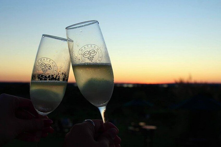Two champagne flutes with 'HATEAU' embossed, held by hands against a sunset background. 4