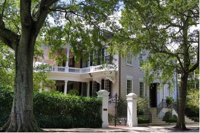 A white building with a balcony, surrounded by trees and a fence. 3