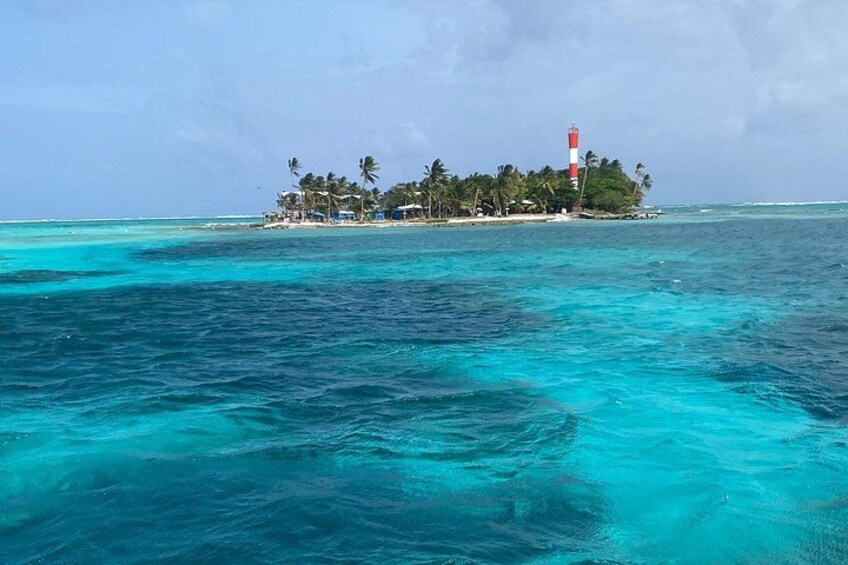 A turquoise sea, a small island with a lighthouse, and palm trees. 5