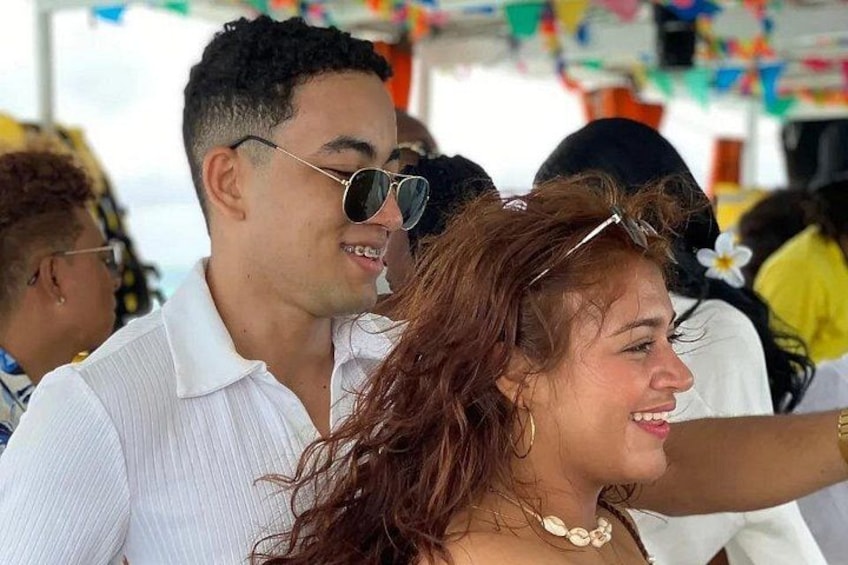 A person wearing a white shirt and sunglasses, another person with a flower accessory, and a colorful tent in the background. 4