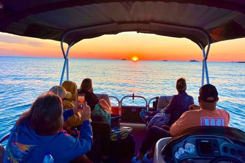 Een zonsondergang boven de oceaan, met een boot en mensen aan boord. 1