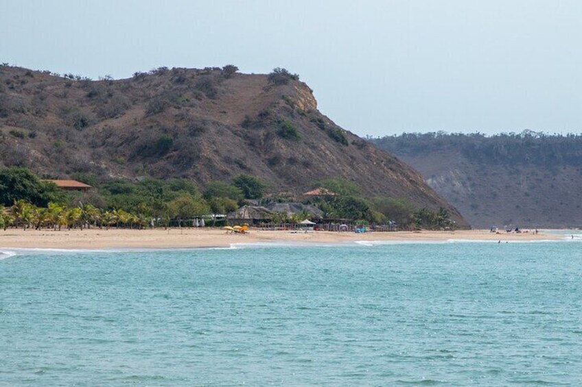A beach with a hill in the background, calm water, and a few people in the distance. 4