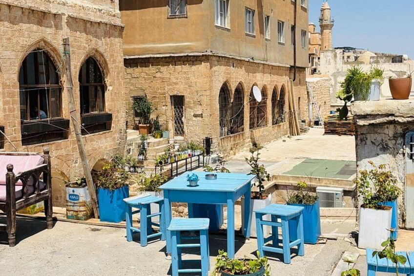 Un patio con mesas y sillas azules, rodeado por edificios de piedra con ventanas arqueadas. 2