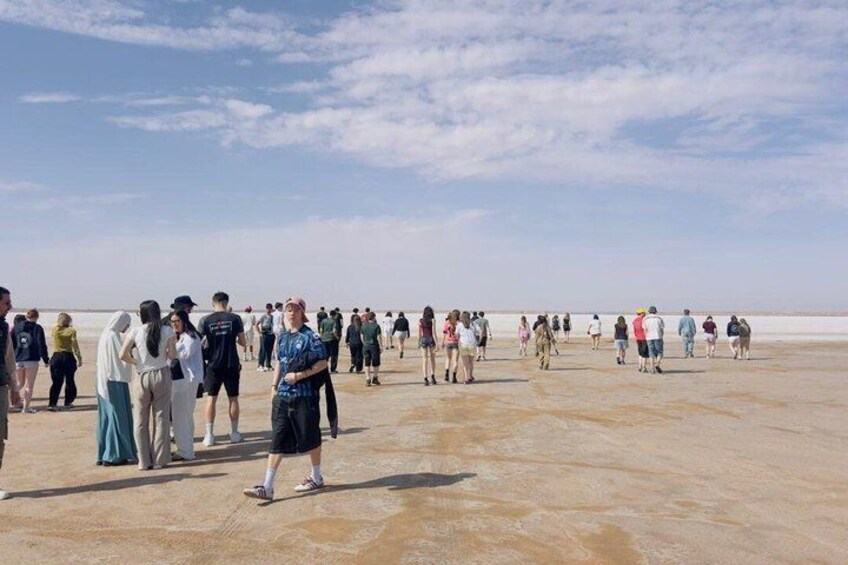 A group of people standing on a flat, expansive salt flat under a clear sky. 2