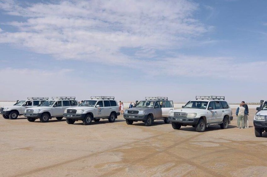 A row of white SUVs parked on a sandy surface under a clear sky. 3