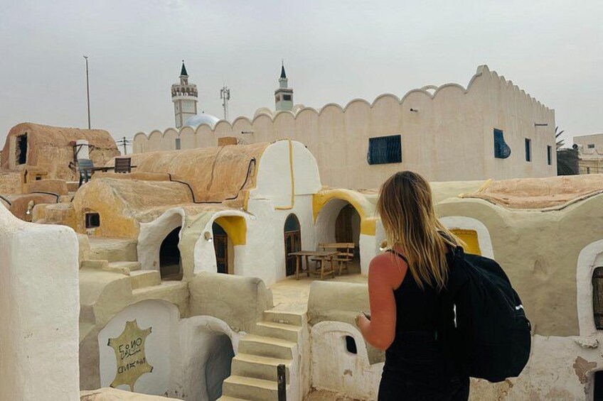 A person standing on a rooftop with traditional architecture, including arches and a mosque in the background. 5