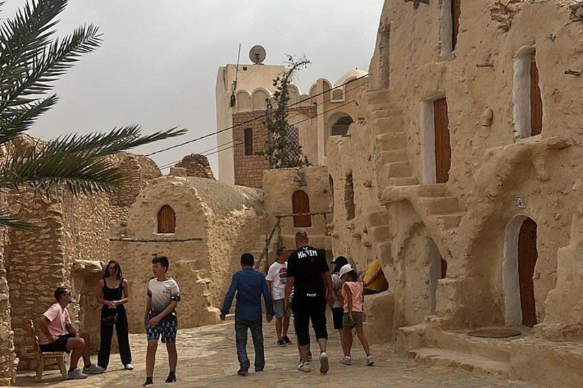 A group of people walking in a historic stone building with arches and a palm tree. 3