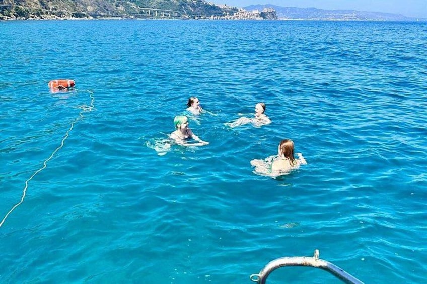 A group of people swimming in a clear blue sea with a boat in the foreground. 1