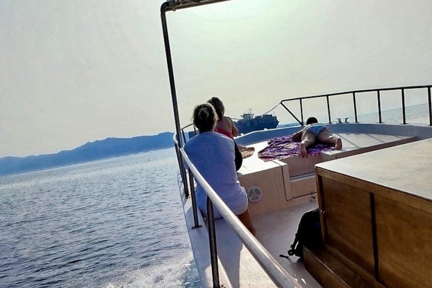 A boat with people relaxing on the deck, a railing, and a view of the water and distant mountains. 4