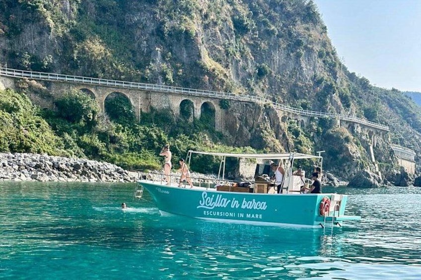 A boat named 'Sejillar in Barca' with people on board, a bridge in the background, and a rocky coastline. 3