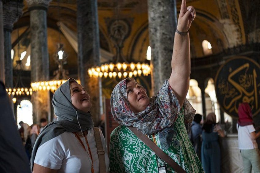 A person pointing upwards in a historical building with ornate columns and intricate wall designs. 1