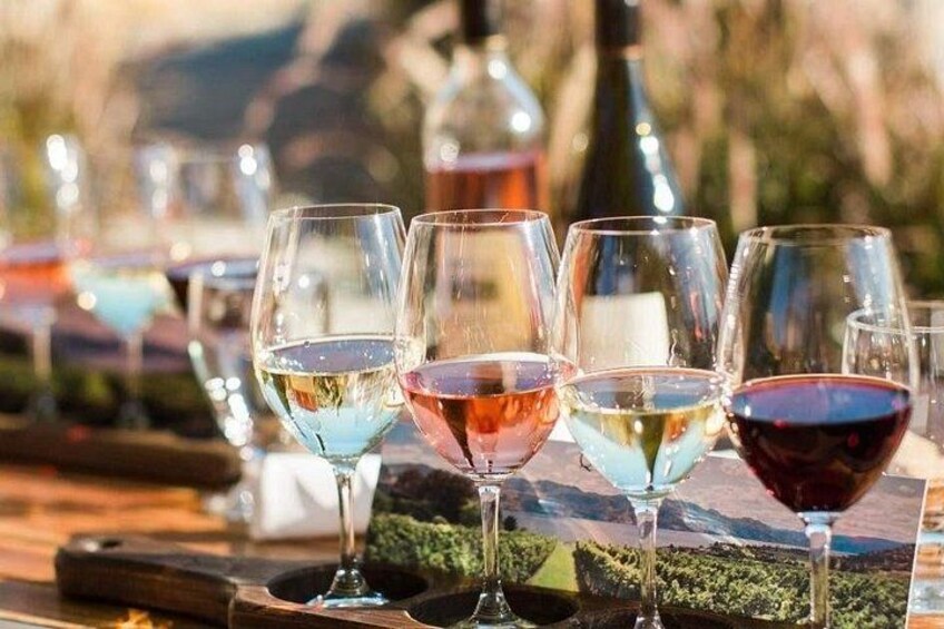 Des verres à vin contenant différents liquides colorés sont posés sur une table en bois, à l’extérieur. 4