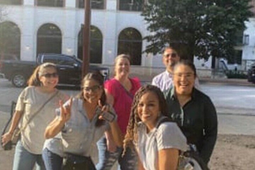 Eine Gruppe von Personen posiert für ein Foto vor einem Gebäude mit Rundbogenfenstern. 1