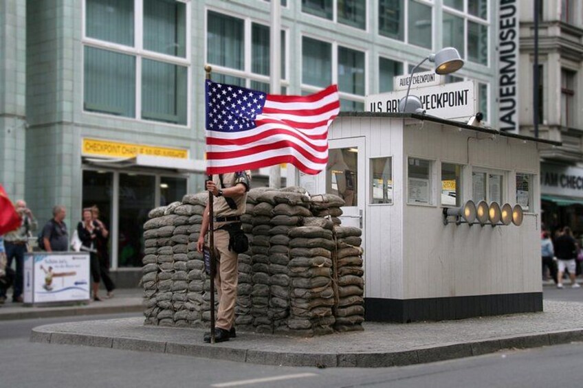 Een soldaat staat naast een stapel zandzakken met een Amerikaanse vlag, voor een gebouw met een bord waarop staat 'MAJOURMUSEUM'. 5