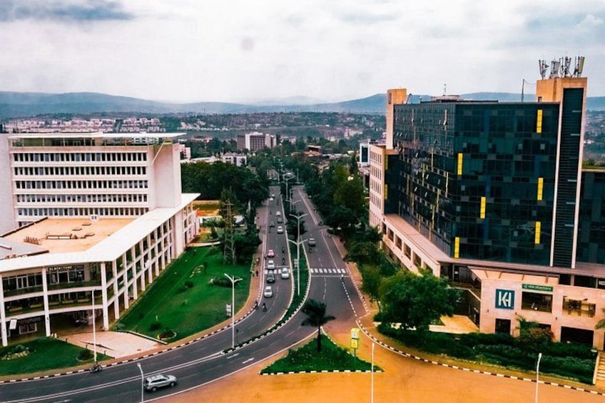 A cityscape with modern buildings, a wide road, and a distant mountain range. 4
