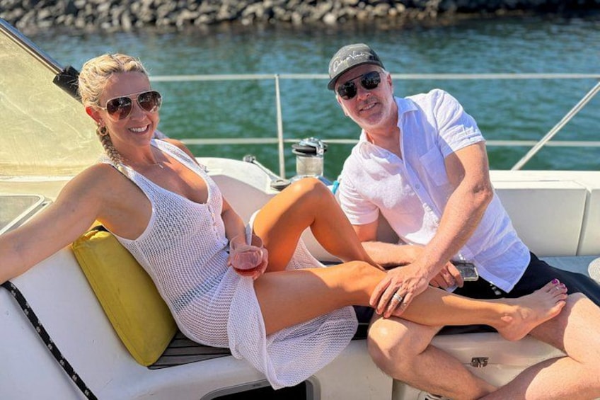 A boat with two people sitting on the deck, a yellow cushion, and calm water in the background. 3