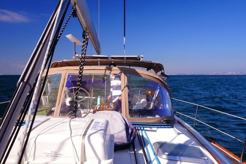 A sailboat with a clear view of the ocean and a distant city skyline. 5