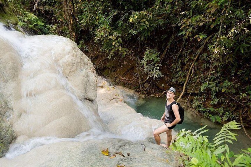 A person standing on a rock by a waterfall in a forested area. 1