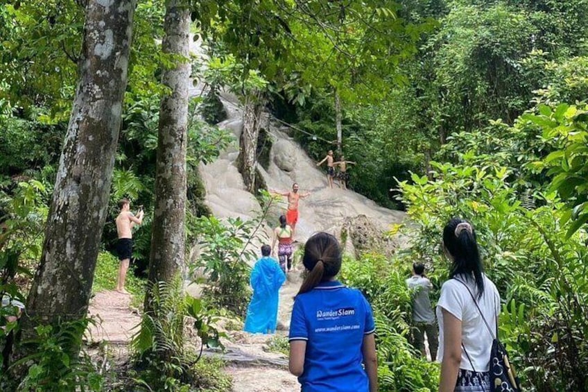 A group of people hiking on a forested trail with a rocky incline. 2