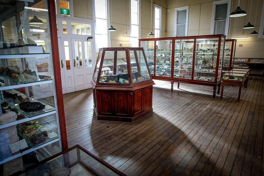 Een museum met houten vloeren, glazen vitrines en een houten kast met glazen deuren. 2