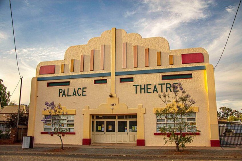 Een gebouw met de aanduiding 'PALACE THEATRE', een kleine boom en een heldere lucht. 3