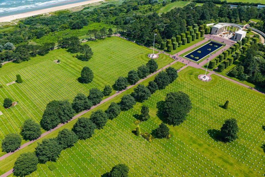 An aerial view of a cemetery with rows of graves, a central pond, and surrounding greenery. 3