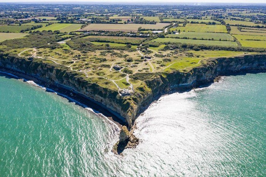 A coastal landscape with cliffs, a narrow waterway, and a distant town. 1