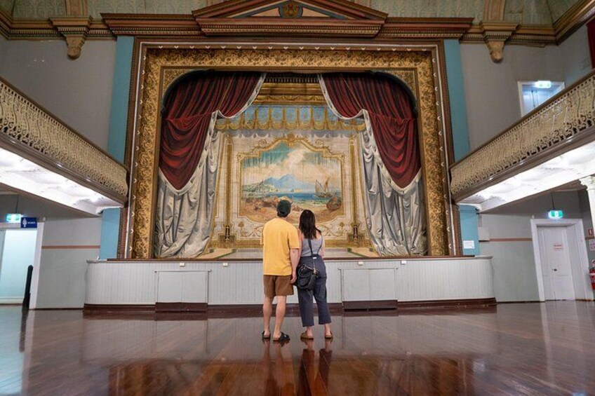 A man and a woman standing in front of a large, ornate stage with a painting. 4