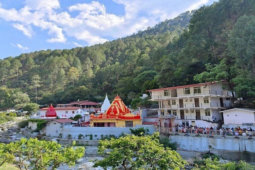 A temple with a red roof, a white building with a balcony, and a forested hillside in the background. 5