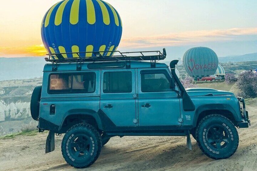 Un SUV azul estacionado en un camino de tierra con un globo aerostático al fondo. 3