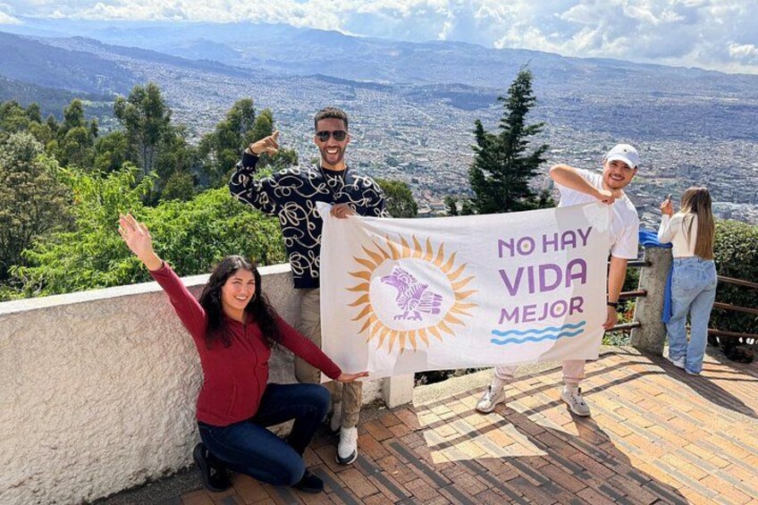 Three people holding a banner with a sun and waves design, standing on a rooftop with a cityscape in the background. 1