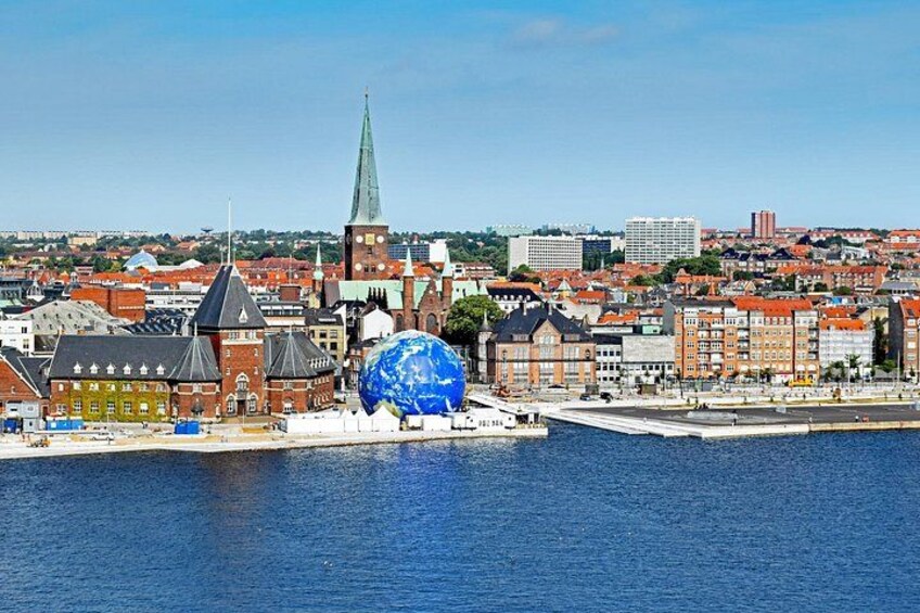 A coastal cityscape with a prominent blue spherical structure, historic buildings, and a church spire. 1
