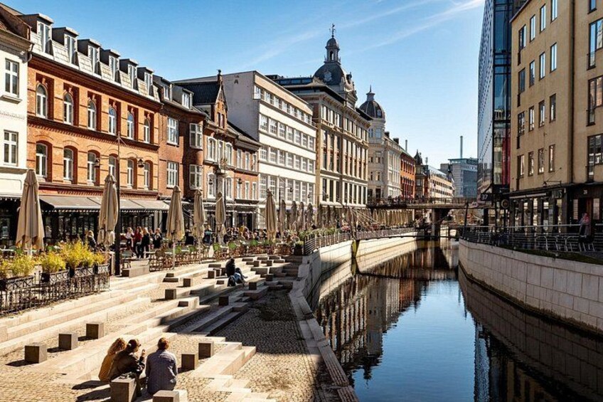 En kanal med trappsteg som leder ner till vattnet, omgiven av historiska byggnader och modern arkitektur. 2