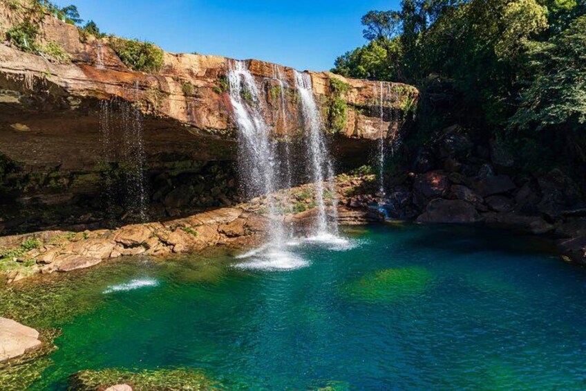 A waterfall cascading into a clear blue pool surrounded by rocky cliffs and greenery. 2