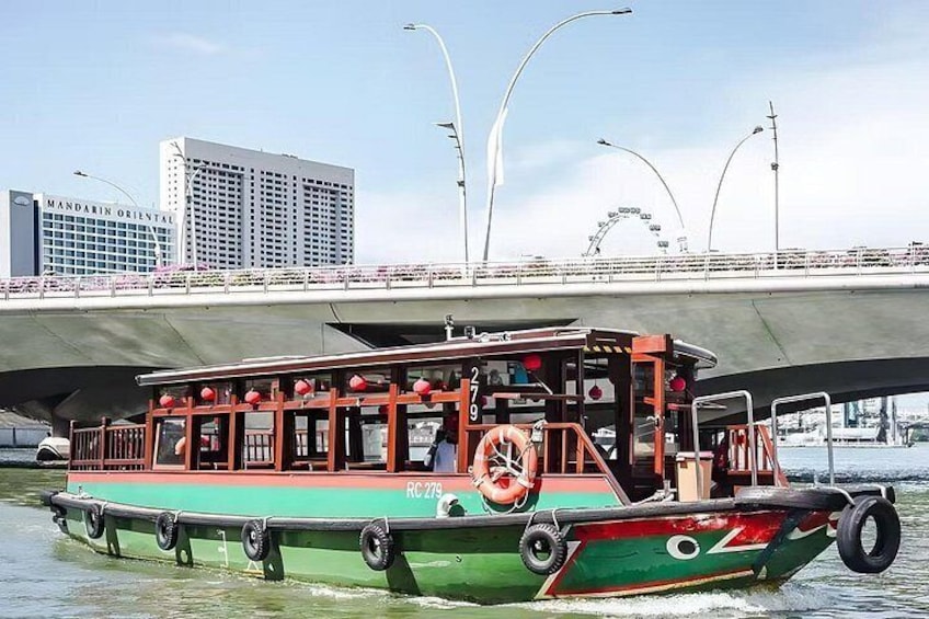 Una embarcación verde y roja con el número RC 279 en un río, bajo un puente con edificios y una noria al fondo. 5