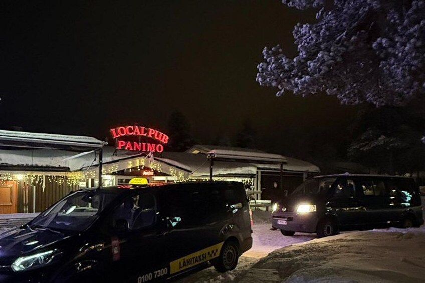 A local pub named 'LOCAL PUB PANIMO' with a neon sign, parked cars, and a snowy ground. 2