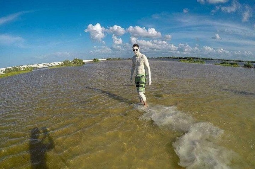 A person standing in shallow water with a clear sky and distant land. 5