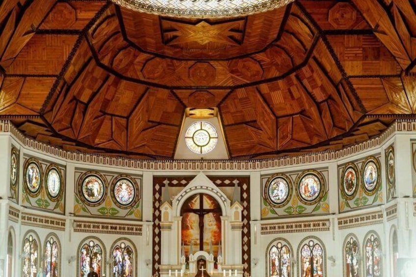 A church interior with a wooden ceiling, stained glass windows, and a central altar. 2