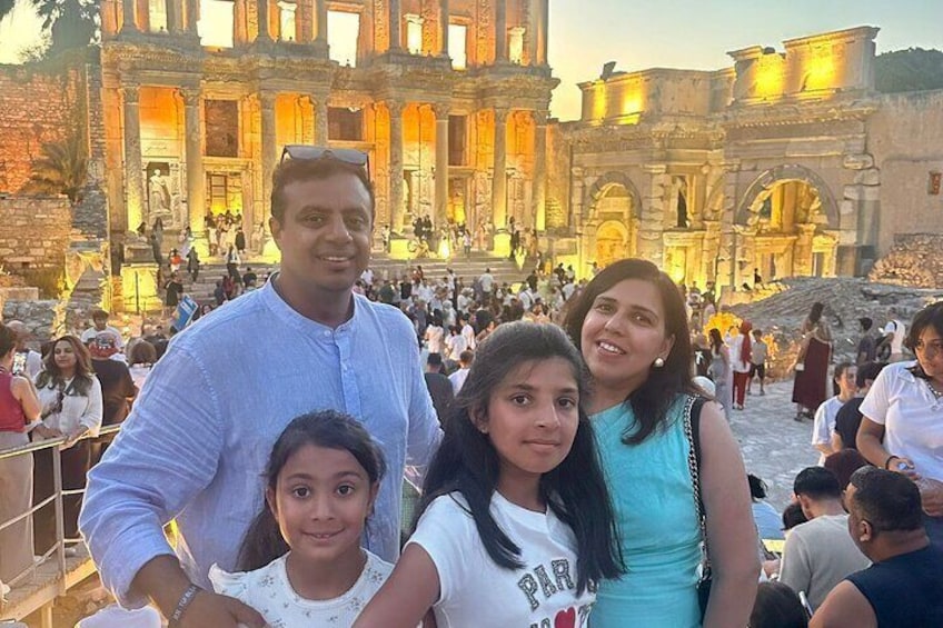A family in front of an ancient ruin with columns and arches, surrounded by other tourists. 5