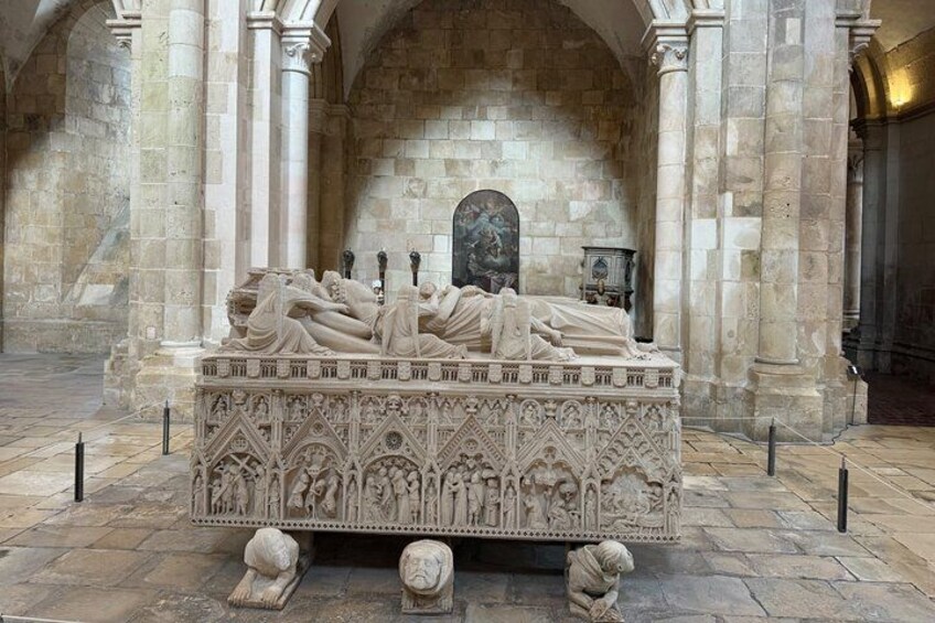 A stone sarcophagus with intricate carvings, set against a stone wall with arches. 2