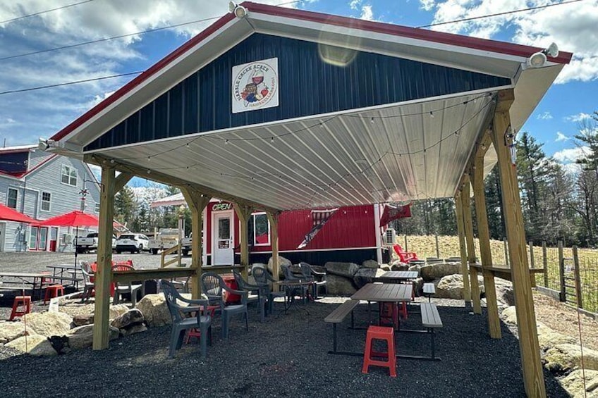 Un espace extérieur abrité, avec des tables et des chaises, un bâtiment rouge en arrière-plan et un sol recouvert de gravier. 4