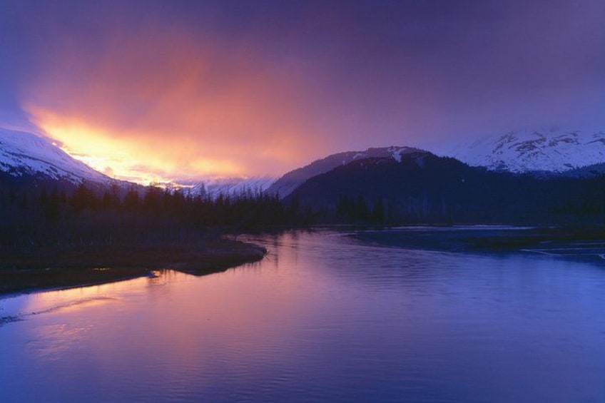 A calm river reflecting a sunset with snow-capped mountains in the background. 2