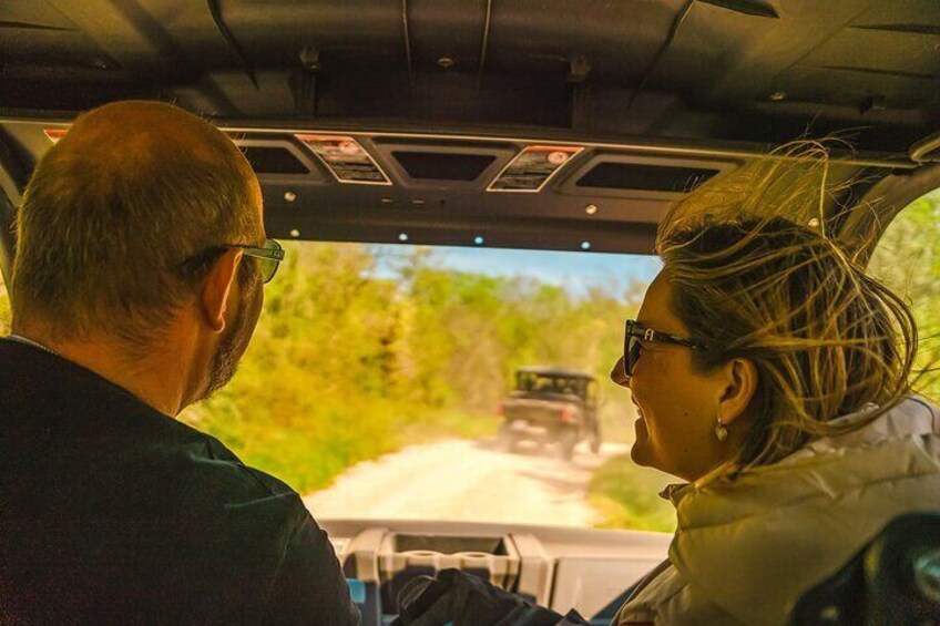 Un homme et une femme conduisent un véhicule sur une route bordée de verdure. 4