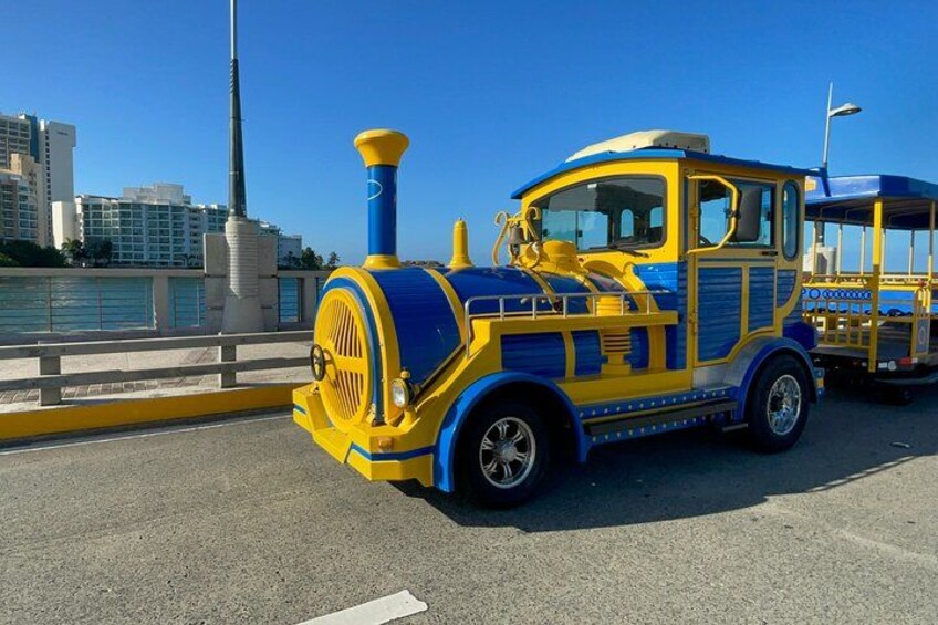 Een blauwe en gele trein op een brug, met gebouwen op de achtergrond. 3