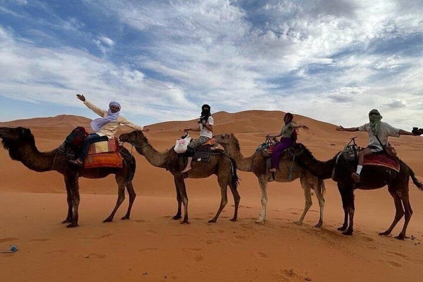 Four camels with riders in a desert landscape. 3